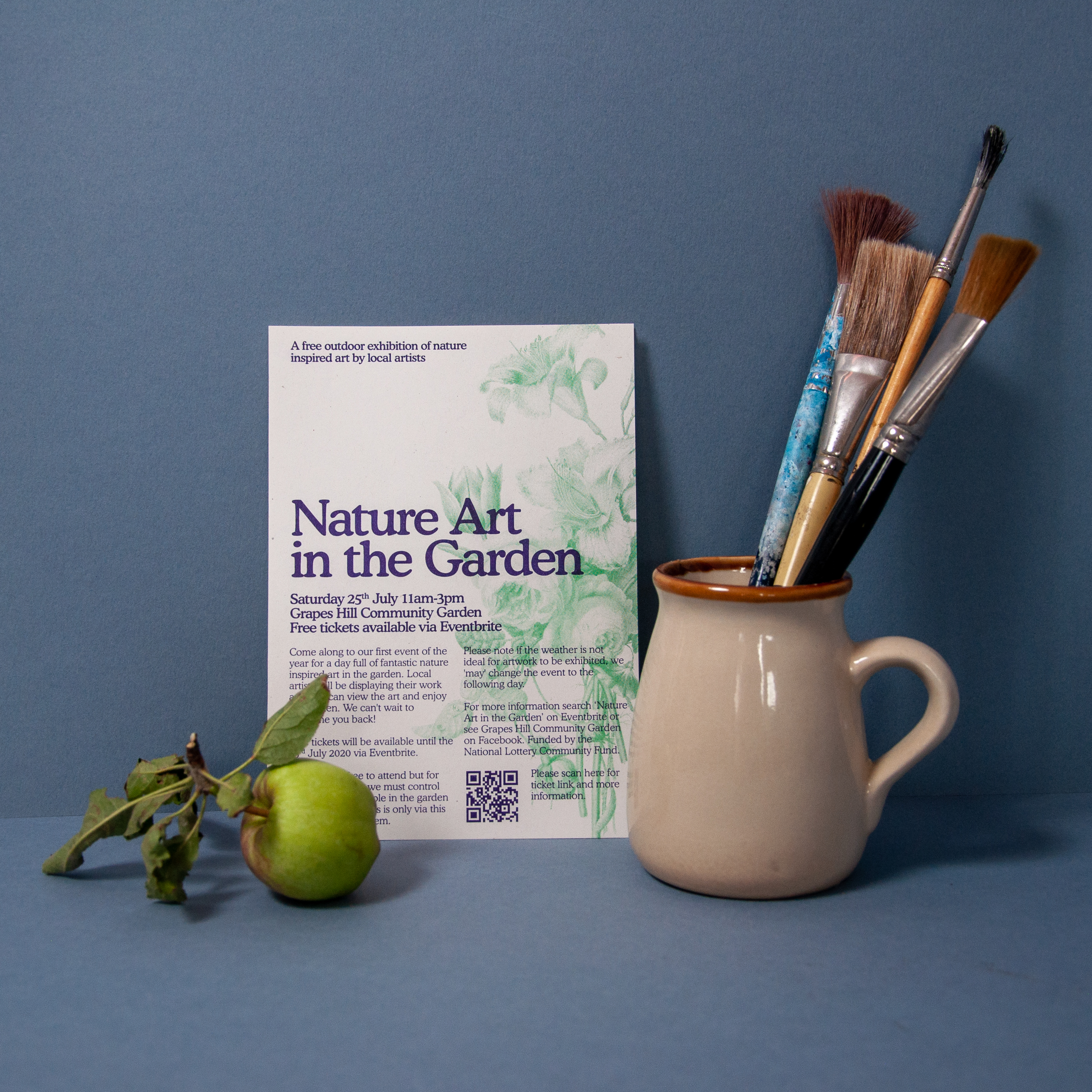 A photograph of a flyer for 'Nature in the Garden', surrounded by an apple and a mug full of paintbrushes.