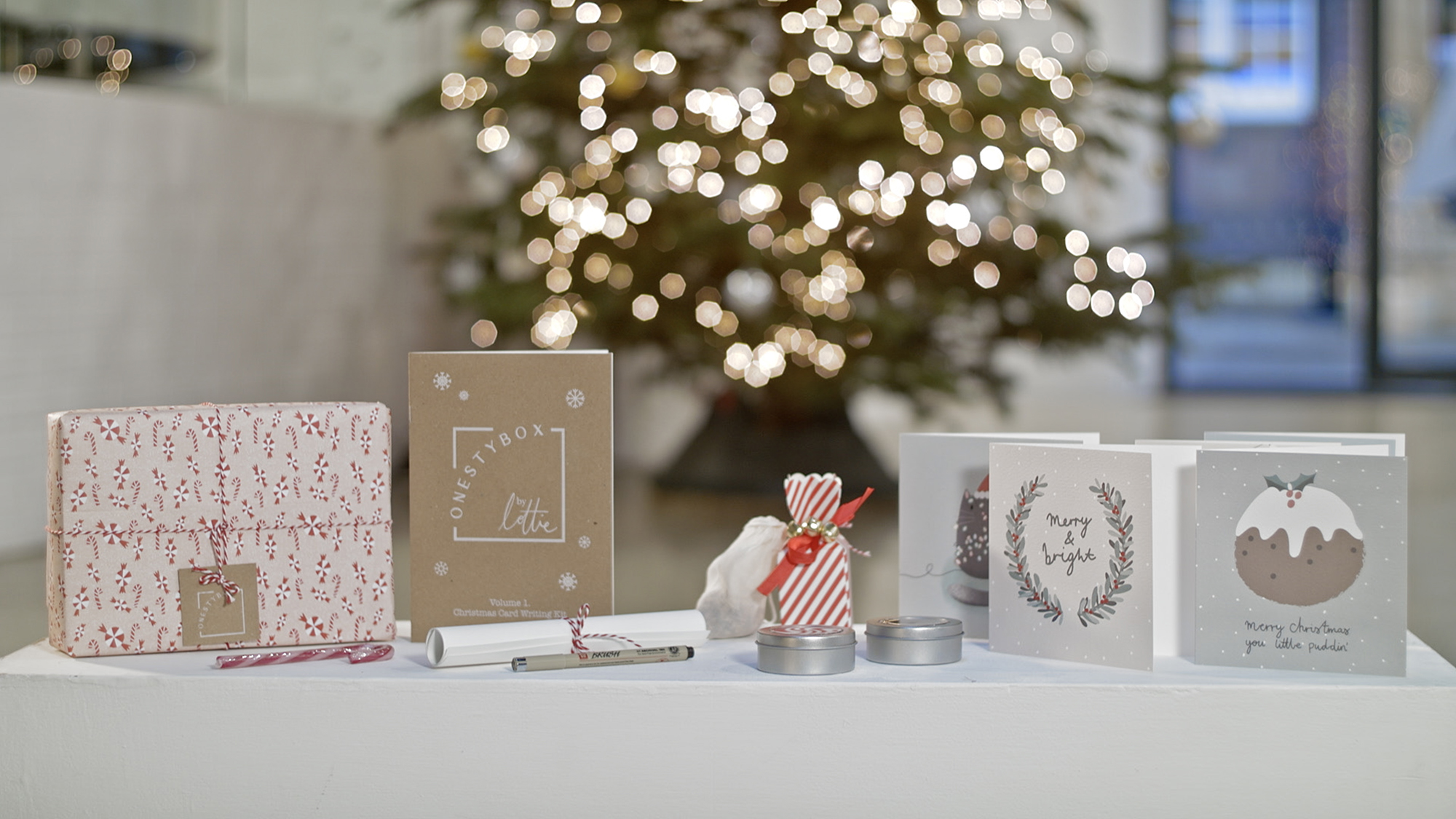 A photograph of a number of items including a booklet with white toner printing, scroll and box in front of a christmas tree.